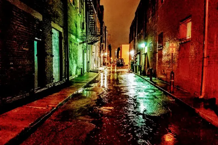 Dark alley dimly lit by lights at night