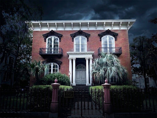 A red-brick house with palm trees and dark, cloudy sky.