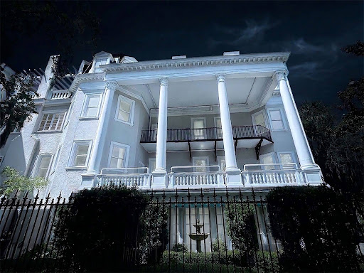 White mansion at night with tall columns and wrought iron fence.